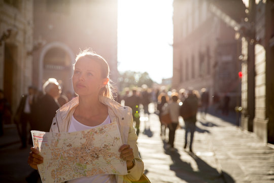 Gorgeous female tourist with a map discovering a foreign city (shallow DOF; color toned image) backlit by warm evening sunshine