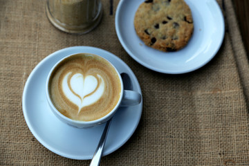 Cappuccino mit Milchschaum in Herzform in Tasse auf Hintergrund Sackleinen