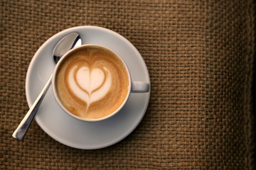 Cappuccino mit Milchschaum in Herzform in Tasse auf Hintergrund Sackleinen