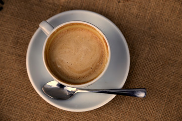 Cappuccino mit Milchschaum in Herzform in Tasse auf Hintergrund Sackleinen