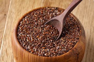 Flax seeds in wooden bowl and spoon on rustic wooden background, top view, shallow depth of field