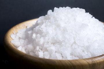 Sea salt white crystals in wooden bowl isolated on the gray background.