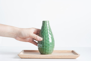 Women's hand holding a green vase on bamboo tray