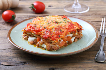 lasagna tradizionale italiana con salsa bolognese e parmigiano su sfondo rustico