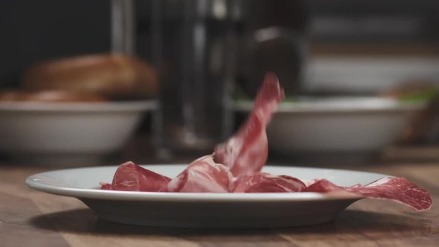 Slow motion of Italian coppa ham falling on white plate closeup