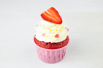 Cupcakes red velvet with white whipped cream decorated with strawberry and confectionery sprinkles in form of heart on white wood table. Picture for a menu or a confectionery catalog.