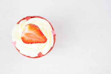 Cupcakes red velvet with white whipped cream decorated with strawberry and confectionery sprinkles in form of heart on white wood table. Picture for a menu or a confectionery catalog.