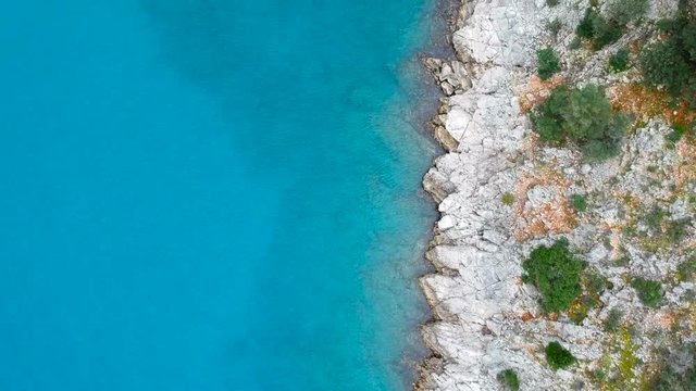 Aerial view looking straight down onto rocky cliffs on a clear turquoise coastline moving over submerged rocks
