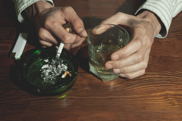 Alcohol abuse, Hands of alcoholic man holding a glass with alcohol drink with smoking cigarette in the ashtray for addiction concept