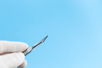 Scalpel in doctors hands in white medical gloves isolated on blue background copy space