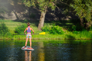 Young athletic woman doing fitness on a board with an oar on a lake