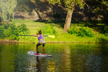 Fototapeta na wymiar Young athletic woman doing fitness on a board with an oar on a lake