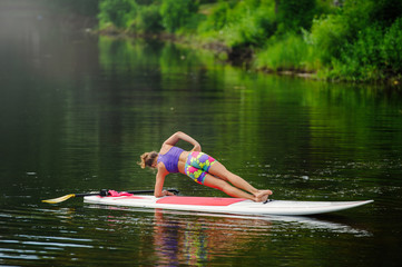 Young athletic woman doing fitness on a board with an oar on a lake
