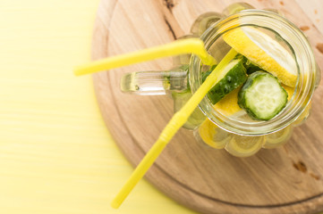 water with lemon and cucumber on a yellow background. concept of detox