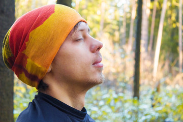 Young man with closed eyes close up in forest. Concept of wellbeing, relaxation and meditation.