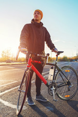 Man stands near a bicycle on the road outdoors. Looks forward to the road