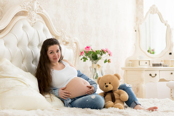 Pregnant girl in the seventh month with difficulty sitting on the bed