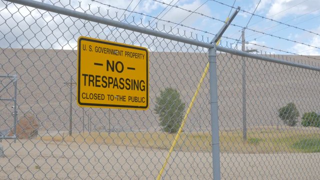 Yellow Sign on a Chain Link Fence Reading U.S. Government Property NO TRESPASSING.