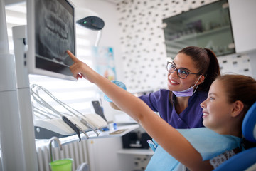 Girl in dental chair showing to dentist her tooth on dental x-ray