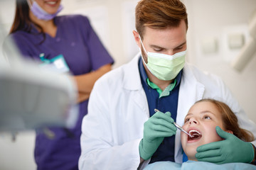 Male dentist examining child's teeth with dental mirror