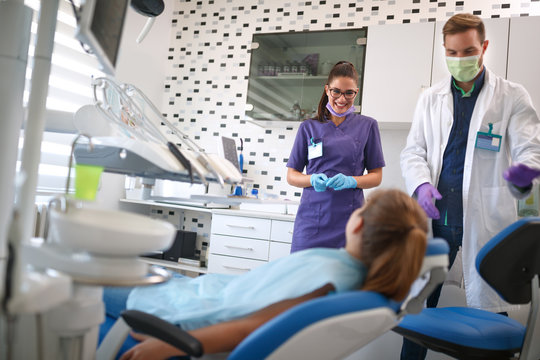 Dental assistant and doctor talking with girl in dental chair