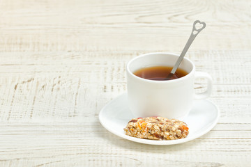 Cup of tea and a bar of muesli. White wooden background