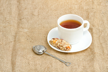 Cup of tea, bar of muesli and tea-strainer on sackcloth