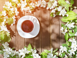 Mug of tea among apple blossom on a wooden background. Top view