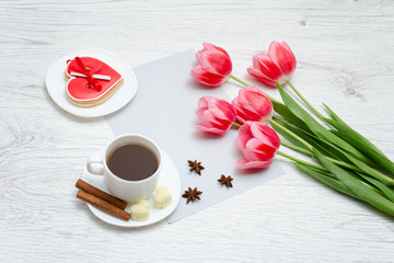 Pink tulips, mug of coffee and red gingerbread. Light wooden background.
