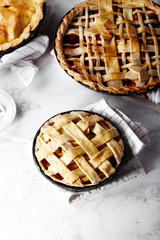 Pie crust design ideas - various ways of pie decoration with lattice and leaves. Apple, strawberry and raspberry pies cooked and served with tea on white marble table