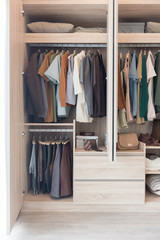 clothes hanging on rails in wooden wardrobe