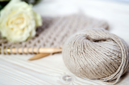 Horn of Merino wool yarn on a wooden surface. In the background a white flower lies on the knitting.
