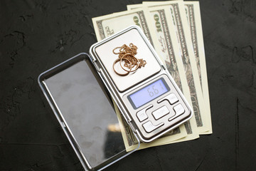 Gold jewelry on the scales and money on a black background
