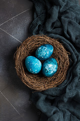 Easter eggs in nest painted by hand in blue color on dark background