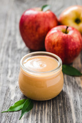 Sugar free applesauce in glass jar and red ripe apples on rustic wooden background. Selective focus, space for text. 