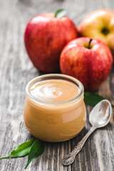 Healthy sugar free applesauce in glass jar and red ripe apples on rustic wooden background. Selective focus, space for text. 