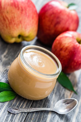 Baby food, applesauce in glass jar and red ripe apples on rustic wooden background. Selective focus, space for text. 