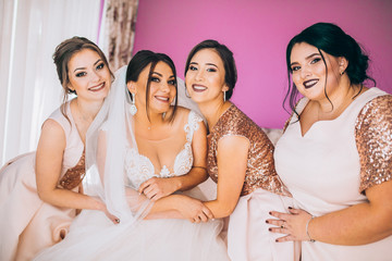 Obraz premium Last details. Full length of two attractive young women adjusting a wedding dress on a beautiful bride. Bridesmaids morning in hotel room. Laughing people.