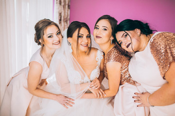 Obraz premium Last details. Full length of two attractive young women adjusting a wedding dress on a beautiful bride. Bridesmaids morning in hotel room. Laughing people.