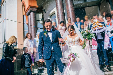 Guests Throwing Confetti Over Bride And Groom At Wedding. Newlyweds walking.