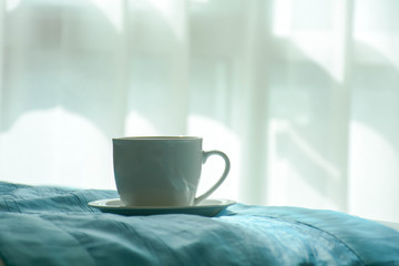 Fototapeta na wymiar white coffee cup on the bed in the morning