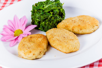 Three fish cutlets with stewed spinach on white plate