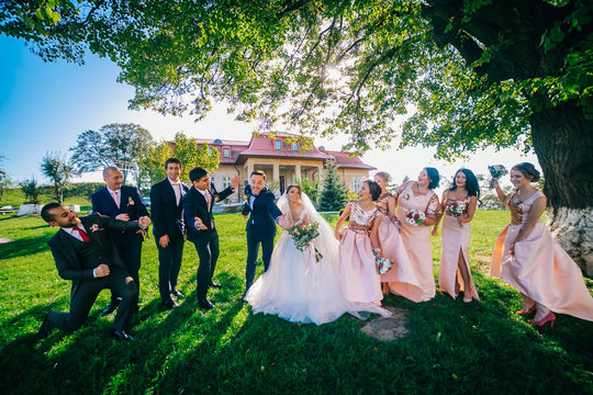 Newlywed couple, bridesmaids & groomsmen having fun outdoors. Bride and groom with best friends posing at sunny green park. Summer picture.