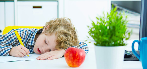 Tired schoolboy writes in a notebook during lesson lying on a table.