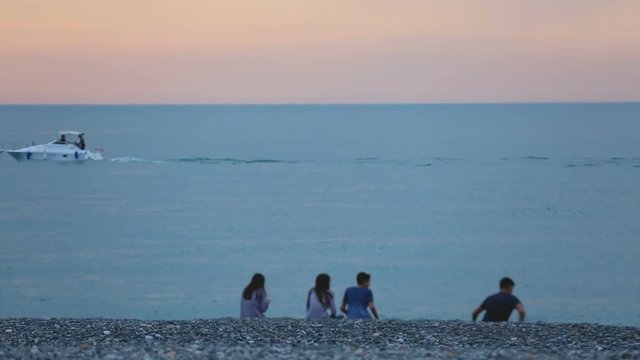 Carefree young friends having fun on pebble beach at dusk, relax at seaside