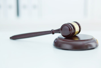 Brown wooden judge gavel lies on a wooden plate on white table.