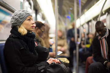 Beautiful blonde caucasian lady wearing winter coat traveling by metro in rush hour. Public...