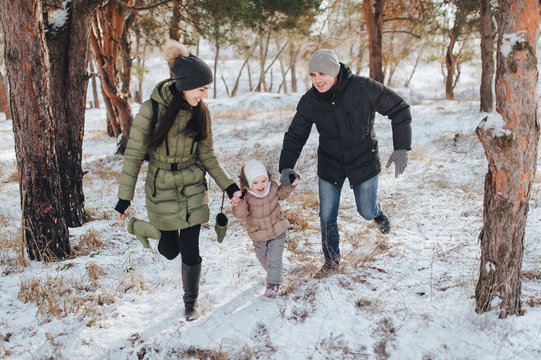 Portrait of Young family and his baby in a winter park. Beautiful daugther. Joke photography. Comic picture. Dad, mom and their little daughter are running, holding hands and laughing cheerfully.