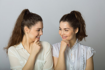 two beautiful smiling girl sisters twins in white blouses on a light background