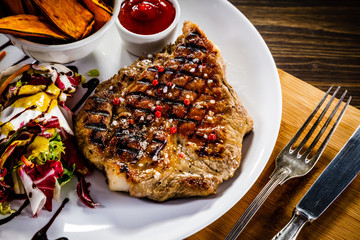 Grilled beefsteak with baked sweet potatoes ad vegetable salad on wooden table